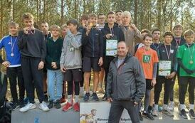 Obraz przedstawia tereny leśne na k&oacute;trych znajduje się grupa chłopc&oacute;w stojących na podium