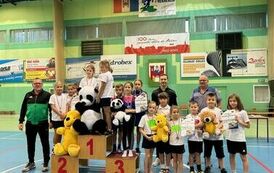 Grupowe zdjęcie dzieci, część znajdująca się na podium z karton&oacute;w oraz część oboch nich trzyma w ręku duże maskotki misi&oacute;w jak puchatek albo pandy