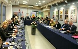 członkowie rady zebrani razem przy stole, po prawej z filiżankami na kawę oraz łakociami, a po prawej panowie i panie z dokumentami