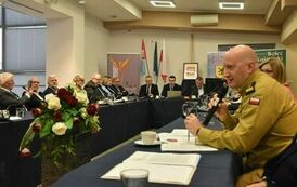 pośr&oacute;d zebranych urzędnik&oacute;w na pierwszym planie przemawia pułkownik 