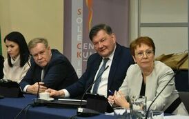 grupka dw&oacute;ch pan&oacute;w i dw&oacute;ch pań siedzi przy stoliku i patrzy zdziwiona 