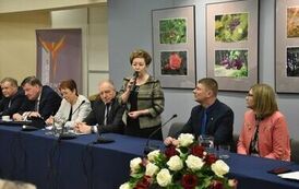 część członk&oacute;w od strony stolik&oacute;w z odą, po środku zgromadzonych soi pani z mikrofonem w zielonej koszuli z czarnymi paskami oraz czarnej sukni