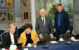 przy stole z rozstawionymi tabletami dwie panie potem jeden starszy pan oraz jeden młodszy. wszyscy ubrani na galowo