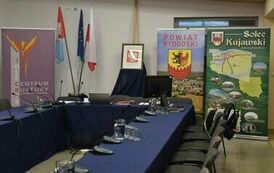 pusty zakrzywiony st&oacute;ł z rozłożonymi na mił dzbankami z wodą oraz z tyłu banery z reklamą Powiatu Bydgoskiego oraz solca kujawskiego 